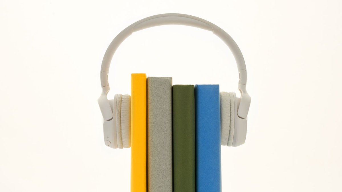 Wei&szlig;e Kopfh&ouml;rer liegen &uuml;ber einer Reihe bunter B&uuml;cher