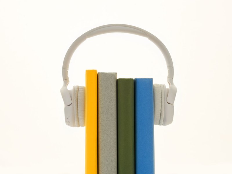 Wei&szlig;e Kopfh&ouml;rer liegen &uuml;ber einer Reihe bunter B&uuml;cher