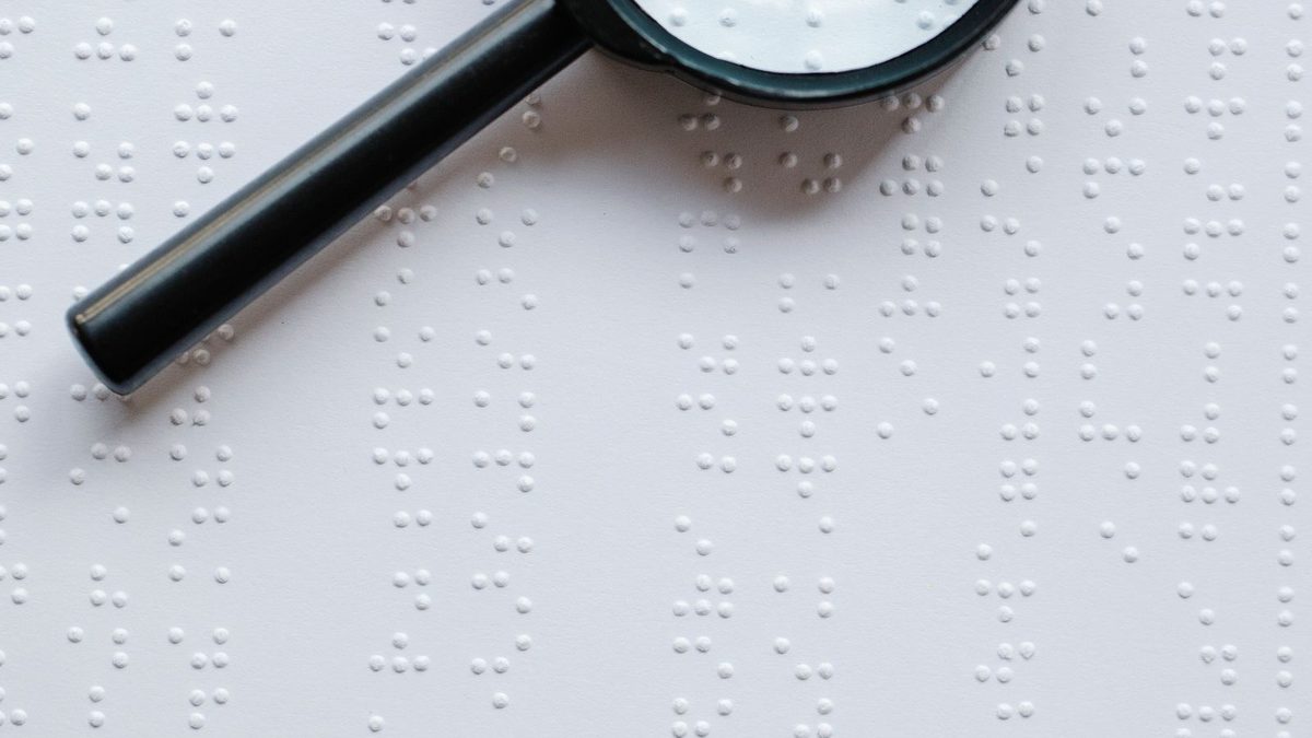 Lupe liegt auf einer Seite mit Brailleschrift