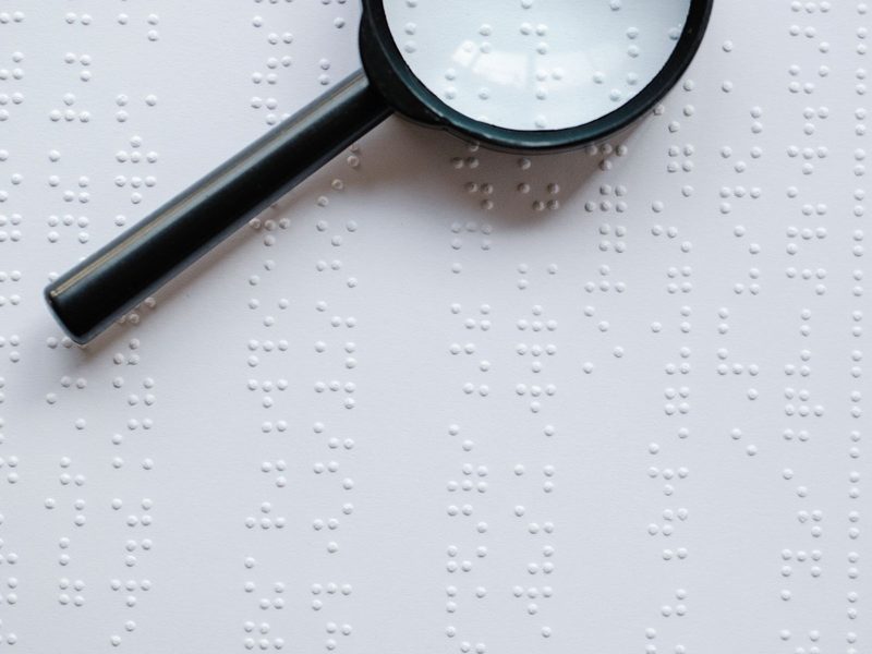 Lupe liegt auf einer Seite mit Brailleschrift