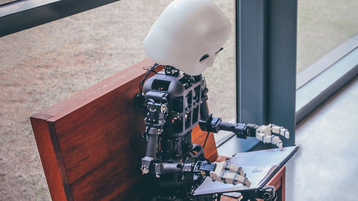 Ein kleiner humanoider Roboter sitzt auf einer Holzbank und bl&auml;ttert in einem Buch