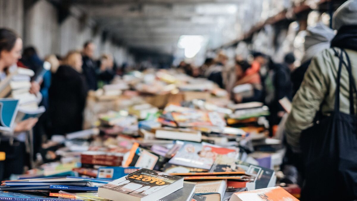 Besucher st&ouml;bern in einer langen Halle an Tischen voller B&uuml;cher