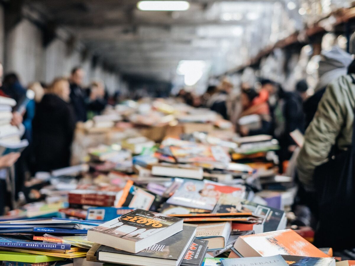 Besucher st&ouml;bern in einer langen Halle an Tischen voller B&uuml;cher