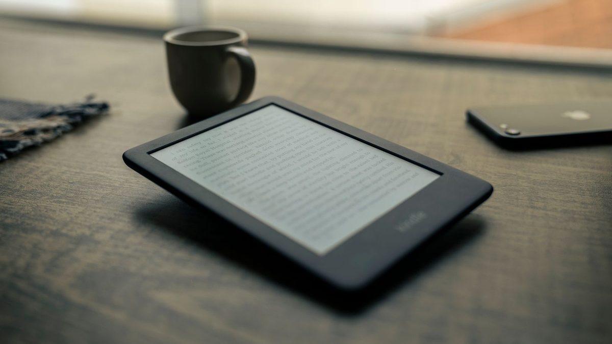 E-Reader liegt auf einem dunklen Holztisch neben einer Kaffeetasse
