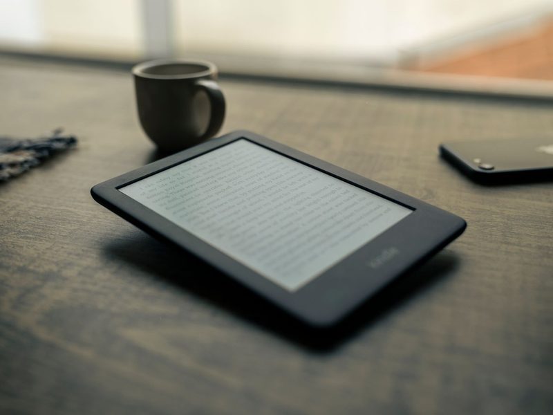 E-Reader liegt auf einem dunklen Holztisch neben einer Kaffeetasse