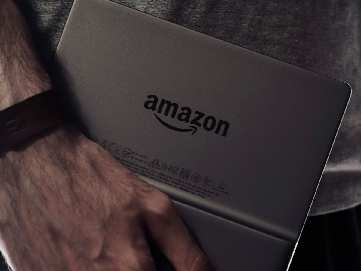 Eine Hand h&auml;lt einen Kindle mit der R&uuml;ckseite und dem Amazon-Logo nach vorn