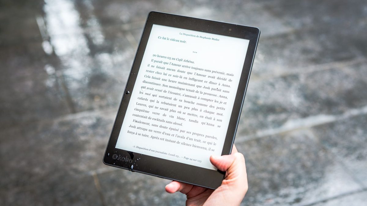 Hand h&auml;lt einen schwarzen E-Reader mit aufgeschlagenem E-Book