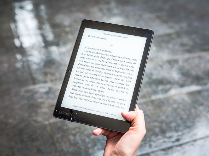 Hand h&auml;lt einen schwarzen E-Reader mit aufgeschlagenem E-Book