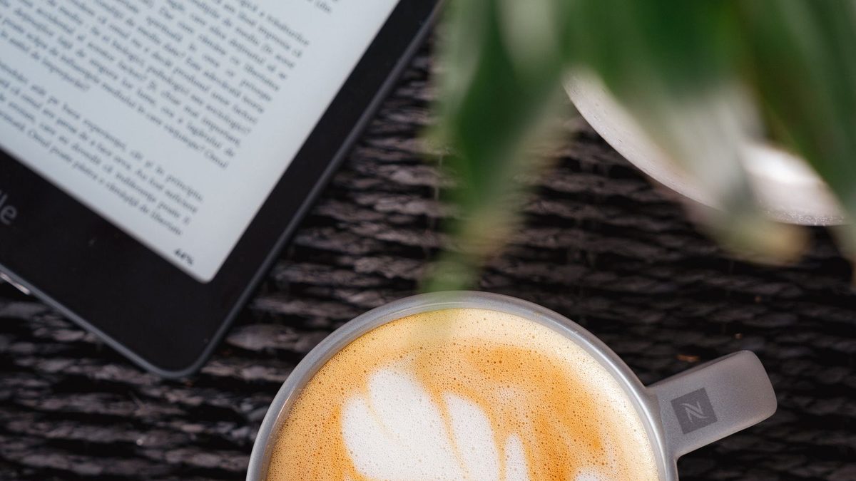 E-Reader und Cappuccino auf einem Tisch, von oben fotografiert
