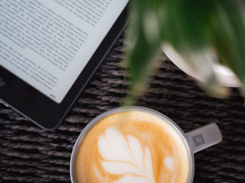 E-Reader und Cappuccino auf einem Tisch, von oben fotografiert