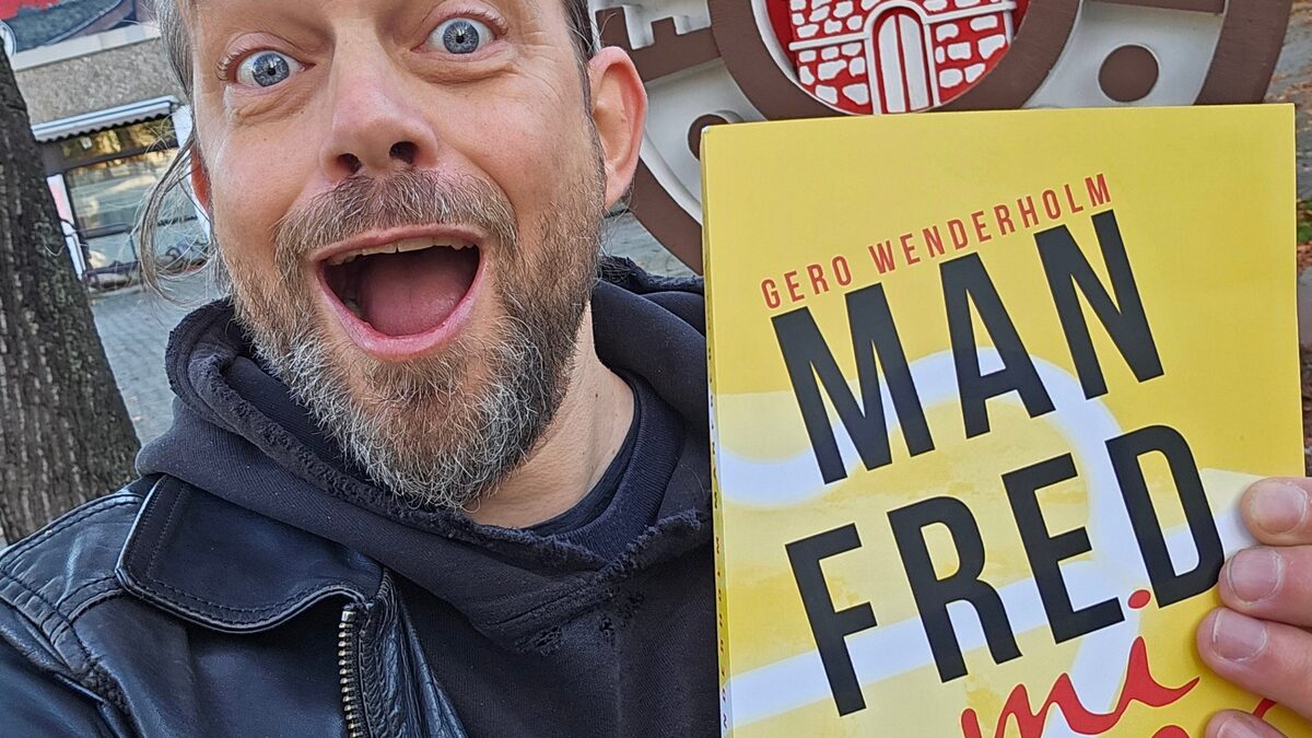 Gero Wenderholm h&auml;lt vor dem Vereinswappen des FC St. Pauli das gelbe Taschenbuch Manfred mi Amor in die Kamera