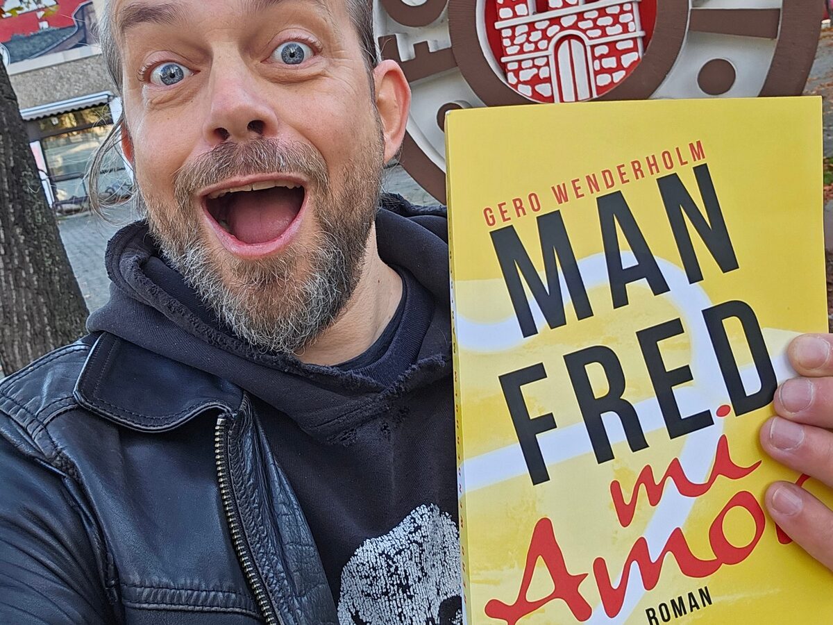 Gero Wenderholm h&auml;lt vor dem Vereinswappen des FC St. Pauli das gelbe Taschenbuch Manfred mi Amor in die Kamera
